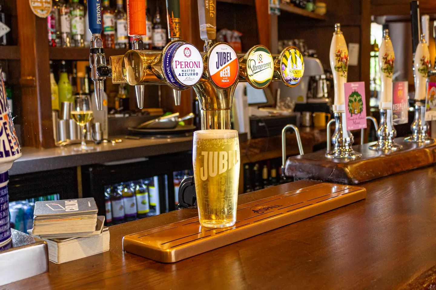 A freshly poured pint of Jubel lager on the drip tray beneath the tap font, hand pulls along the bar