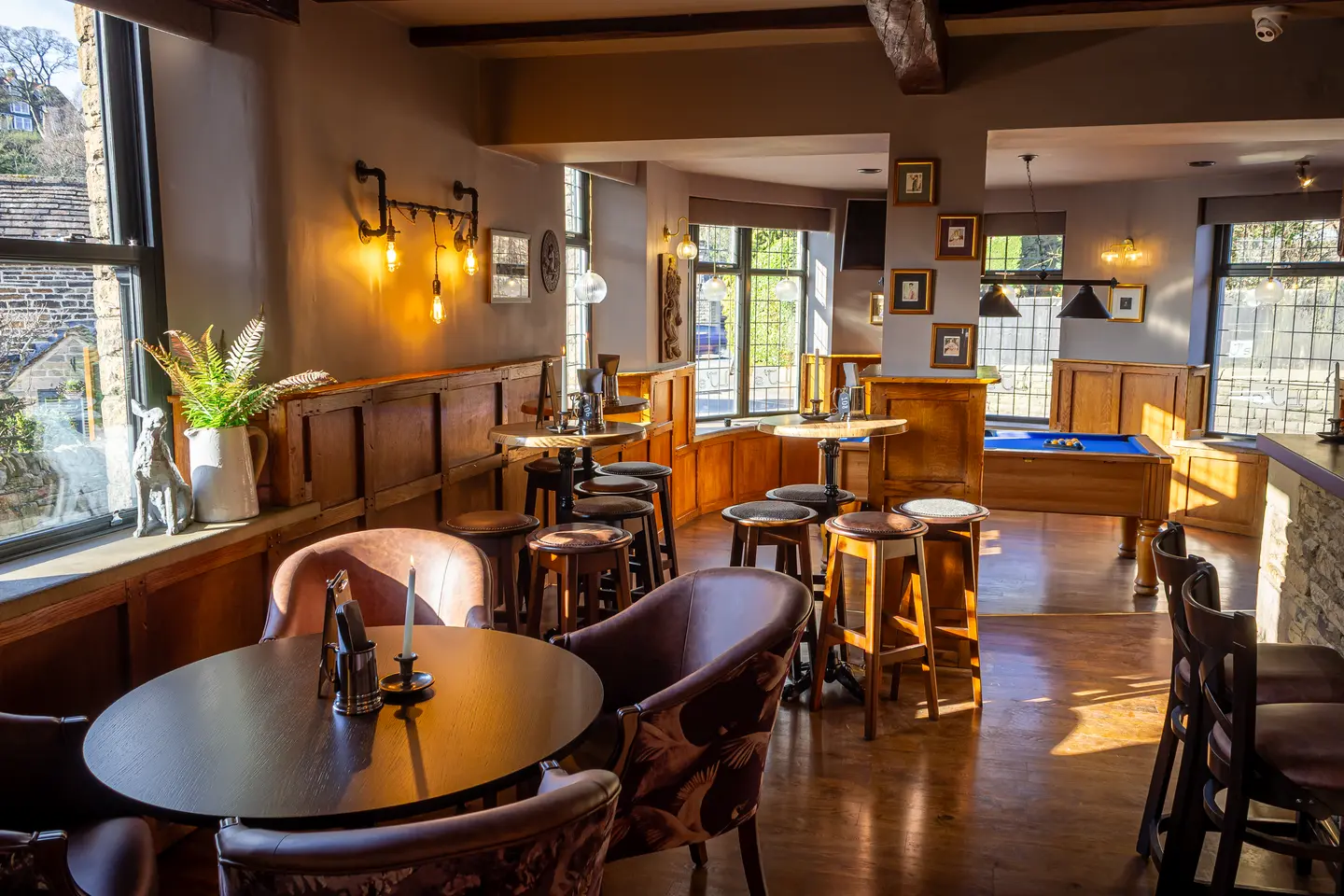 Low sun across the bar room: round tables and tub chairs, high stools at the poseur tables and the pool table beyond