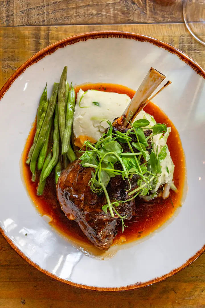 A braised lamb shank with mash and green beans