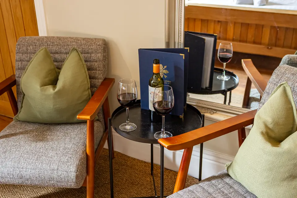 Two armchairs either side of a small table with a bottle of red wine, two glasses and a Little John menu